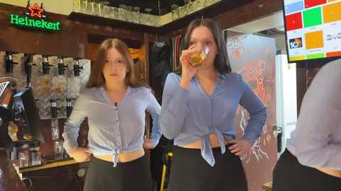 Media: Video of two young women in light blue shirts, black pants, drinking beer in a Heineken bar.