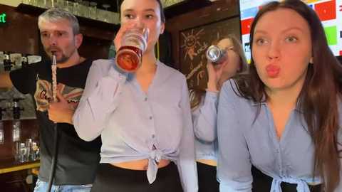 Media: A video of three women in a pub, each holding a glass of beer, wearing light blue tops tied at the waist. Background shows wooden bar and colorful wall art.