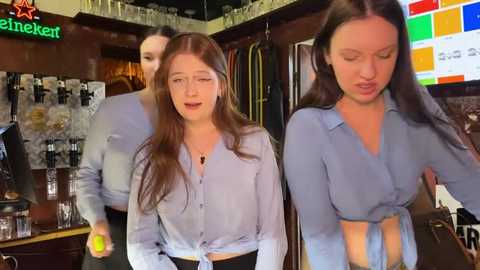 Media: Video of two young women, one tied blouse, in a lively bar with colorful neon lights and shelves of alcohol.