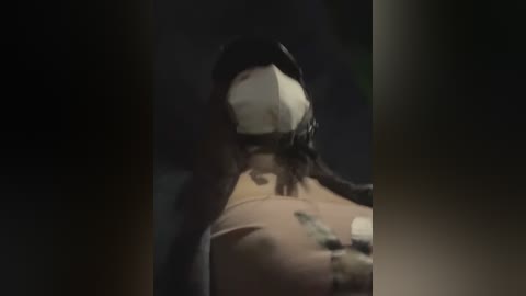 Media: Video of a person wearing a white mask and a dark hooded jacket, viewed from behind, with blurred background.