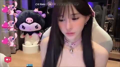 Media: Video of a young woman with long black hair, wearing a white top, and a pink choker, sitting in front of a plush stuffed animal, in a cozy indoor setting.