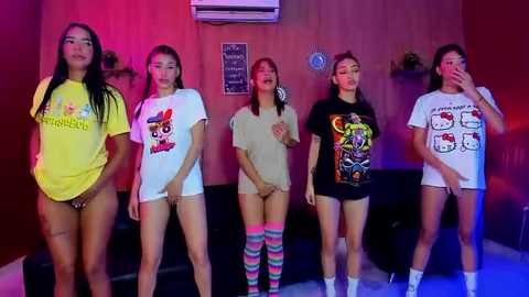 Media: Video of five Asian women in colorful, graphic T-shirts and thigh-high socks posing seductively in a dimly-lit room with red and blue lighting.