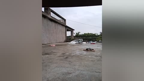 Media: Video of a muddy, debris-strewn area in front of a large, partially collapsed building. The structure has \"BINGKONGAN\" written in white on its wall. A person in dark clothing is partially visible, crouched on the ground.