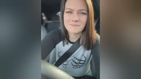 Media: A video of a young woman with shoulder-length, light brown hair and light skin, wearing a Star Wars t-shirt and a seatbelt, seated in a car.