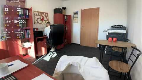 Media: Video of a tidy office with a wooden door, a desk, a chair, red bookshelves, a computer monitor, a calendar, and a white cloth on the floor.