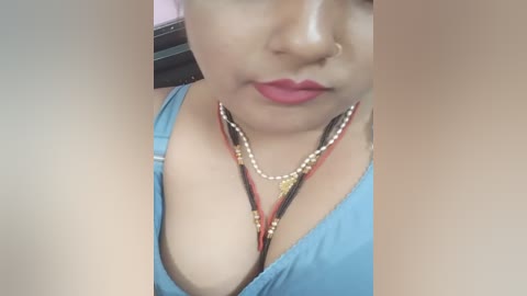 Media: Video of a woman with light brown skin, wearing a blue tank top, showing cleavage, adorned with multiple necklaces.