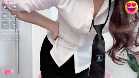 Media: Video of a woman in a white blouse, black tie, and black skirt, standing in a modern room with a white background.