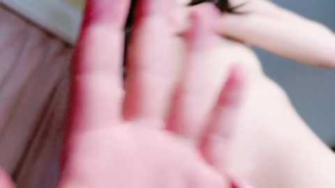 Media: A close-up, slightly blurred video shows a fair-skinned person with dark hair, their hand placed on a wooden surface. The image has a soft, pinkish hue.