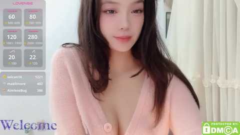 Media: A video of a young East Asian woman with long black hair, wearing a low-cut pink cardigan, smiling softly. The background features a light-colored curtain and a digital display showing 80% occupancy.