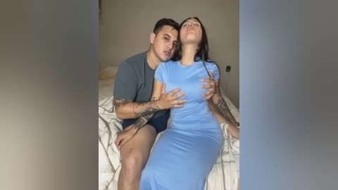 Media: A video of a young couple on a bed, man wearing a gray shirt, woman in a light blue dress, embracing passionately, tattoos visible.