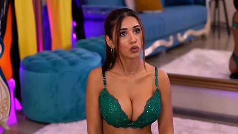 Media: Video of a curvaceous woman with long dark hair, wearing a green sequined bra, in a modern, brightly lit room with teal furniture and colorful accents.