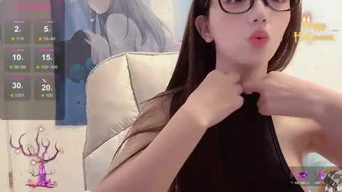 Media: Video of an Asian woman with long brown hair, wearing black-rimmed glasses and a black top, making a pouty face. Background shows a white leather chair and a poster with an anime character.