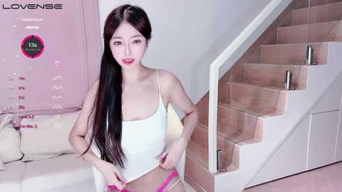 Media: Video of an Asian woman with long black hair, wearing a white tank top and pink panties, standing on a modern white staircase.