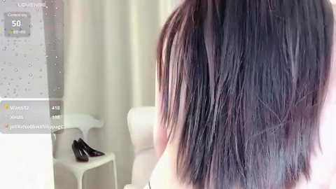 Media: Video of a person's shoulder-length, straight, dark brown hair styled with subtle layers, viewed from behind. Background features a white chair and a black shoe.