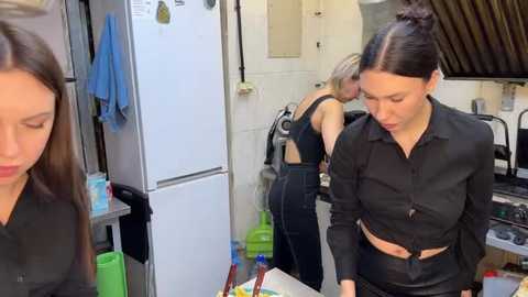 Media: Video of two women in a kitchen: one with long brown hair in a black shirt, another with short blonde hair in a black top, both focused on cleaning.