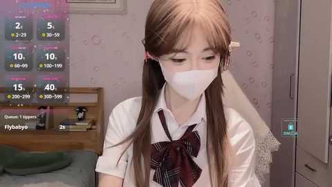 Media: A young Asian woman with long brown hair in a plaid tie, wearing a white shirt, mask, and school uniform, sits indoors.