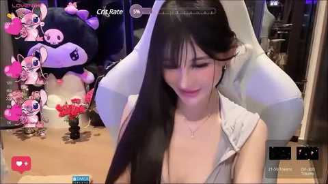 Media: A video of a young Asian woman with long black hair, wearing a sleeveless top, seated in front of a computer screen displaying an animated pink plush character.