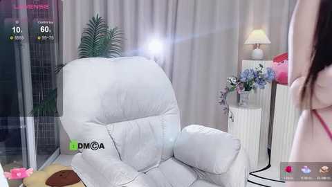 Media: Video of a modern, light-filled room with a white leather recliner, green plant, pink flowers, and a white table lamp.