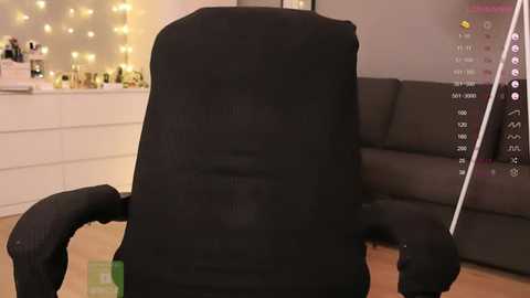 Media: A video of a person in a black, furry onesie sitting in a dark brown leather armchair, with a white dresser and string lights in the background.