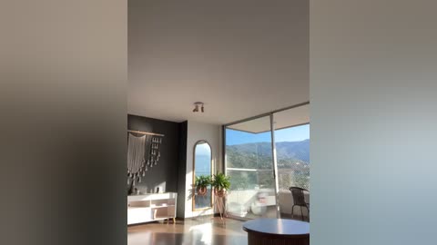 Media: A modern, minimalist living room with large windows, showcasing a lush green landscape and mountains; sleek white walls, a macram\u00e9 wall hanging, and a potted plant.