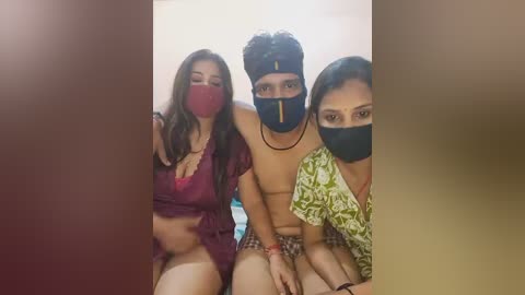 Media: Video of three people in a room: two women and a man, all wearing masks, the man topless, the women in lingerie.