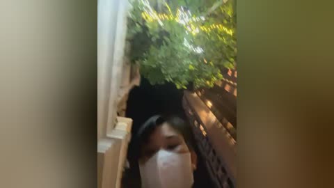 Media: A blurry, close-up video of a person wearing a white mask, standing in a narrow, green-lit corridor with beige walls and a wooden railing.