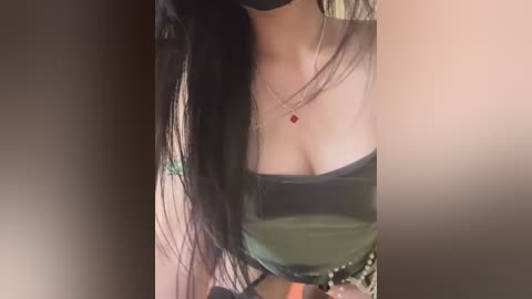 Media: A video of a woman with long black hair, wearing a black strapless top that accentuates her cleavage, a red pendant necklace, and a black mask.