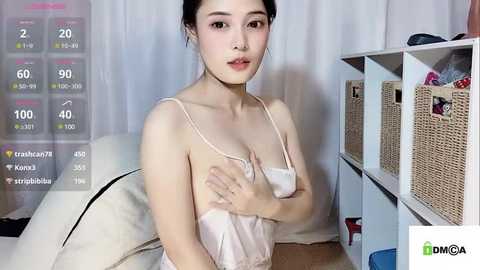 Media: A video of an Asian woman with light skin and dark hair, wearing a pink camisole, in a room with white curtains and a wicker storage bin.