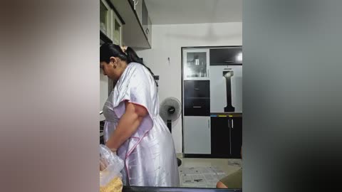 Media: A video of a woman in a white apron, standing in a modern kitchen with stainless steel appliances, white walls, and a fan.