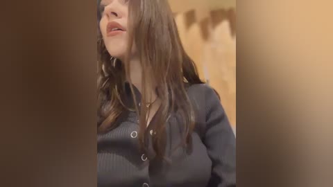 Media: Video of a young woman with long, wavy brown hair, fair skin, and a black cardigan, looking downward, blurred background.