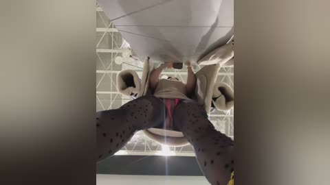 Media: Video of a person wearing a pink thong, standing inside a modern, white, angular building with large, circular windows, viewed from below, emphasizing the legs and underwear.