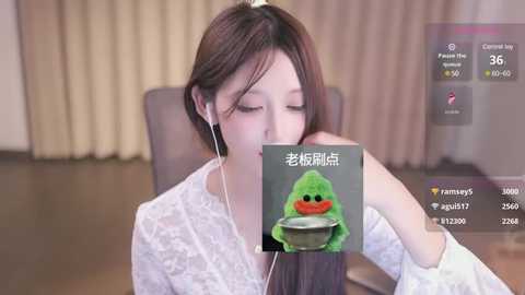 Media: Video of an Asian woman with short brown hair, wearing headphones, drinking soup from a green bowl. She's in a modern, well-lit room with beige curtains.