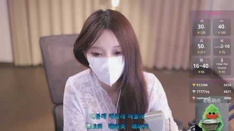 Media: Video of an Asian woman with long brown hair and a white surgical mask, wearing a white lace dress, sitting indoors, surrounded by Chinese text and a green frog emoji.