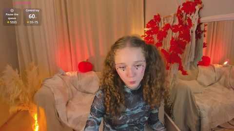 Media: A video of a young girl with curly hair in a dark blue striped top, seated in a room with festive decor, including red ribbons, a pumpkin, and warm lighting.