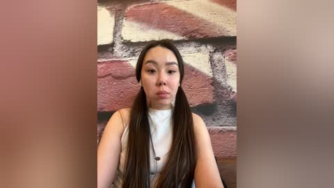 Media: Video of an East Asian woman with long, straight black hair parted in the middle, wearing a white turtleneck. She stands against a textured, brick-like wall.