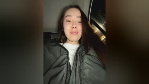 Media: A video of an Asian woman with long black hair, closed eyes, and a pouty expression, wearing a dark jacket over a white shirt, sitting in a car.