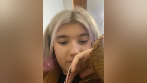 Media: A video shows a young woman with light skin and pastel pink hair, applying makeup with a black lipstick. She wears a brown, textured jacket.