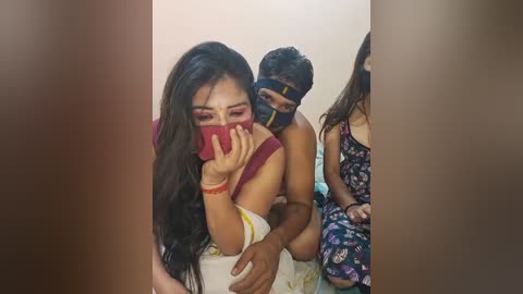 Media: Video of a distraught South Asian woman with long hair, wearing a red mask, held by a muscular man in a black mask.