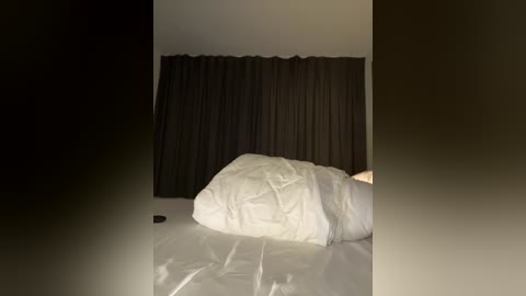 Media: Video of a minimalist bedroom with a white bed, black curtains, and a dark, shadowy background, creating a moody, serene atmosphere.