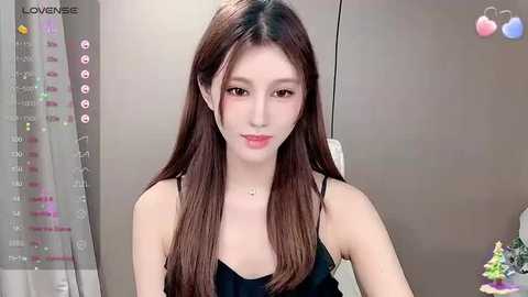 Media: A video of a young East Asian woman with long, straight brown hair, wearing a black spaghetti-strap top, standing indoors against a gray background.