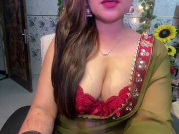 Media: Video of a South Asian woman with fair skin, wearing a green saree with red lace bra, gold jewelry, and a floral background.