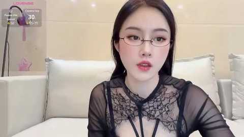 Media: A video of a fair-skinned, young Asian woman with long dark hair, wearing black lace lingerie and glasses, sitting on a white bed.