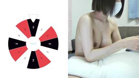 Media: Video of a topless Asian woman with short black hair, medium breasts, and fair skin, sitting on a bed. Next to her is a dice-like spinner with red and black segments.