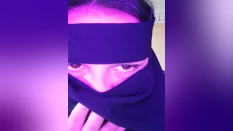 Media: A video of a person with light skin and dark hair, wearing a black headband and robe, set against a purple backdrop, creating a dramatic, mysterious atmosphere.