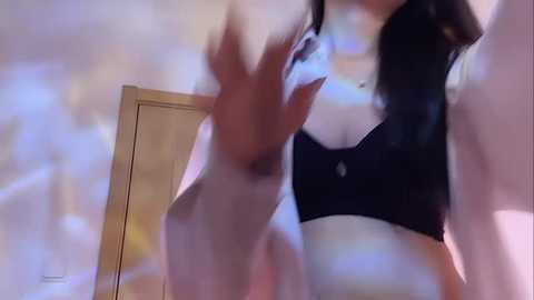 Media: Video of a woman with pale skin and black hair, wearing a black bra, caught in motion with a blurred background.