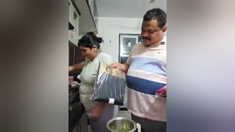 Media: Video of a woman in a white top and man in a striped shirt, both with medium skin tones, standing in a kitchen, preparing food.