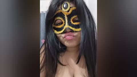 Media: Video of a young woman with long black hair, wearing an elaborate black and gold masquerade mask, kissing her cheek. She is topless, with a visible collarbone.