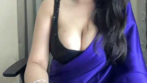 Media: A video of a woman with long, dark hair, wearing a black bra and a vibrant blue sari, sitting indoors with blurred background.