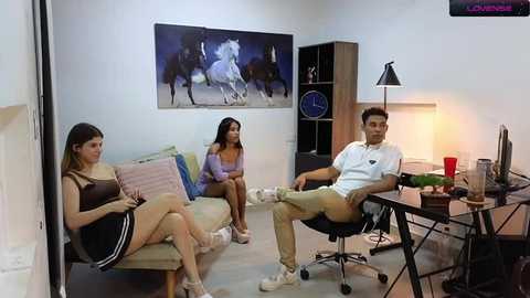 Media: Video of a casual living room with three people: two women in casual attire and a man in a white shirt and beige pants, sitting on a couch and chairs.