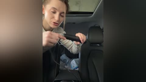 Media: Video of a woman with light skin and brown hair in a car, adjusting a black car seat belt while wearing white earbuds, sitting in the passenger seat.